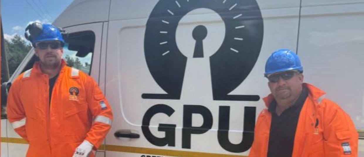 Two Green Power Utilities crew members in orange hi-vis and hard hats beside a branded GPU van.